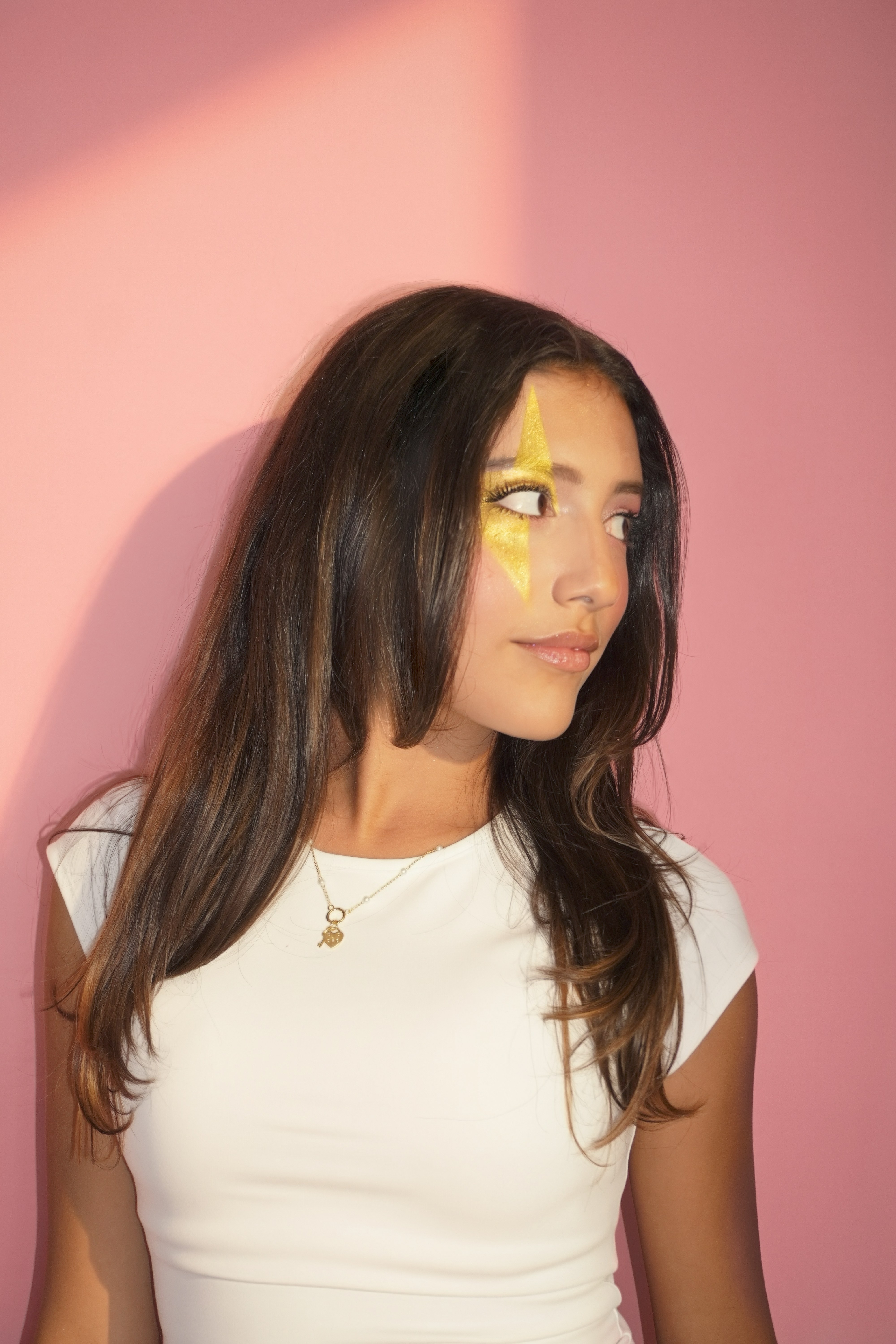 Naty G close-up with gold lightning makeup against a pink background.